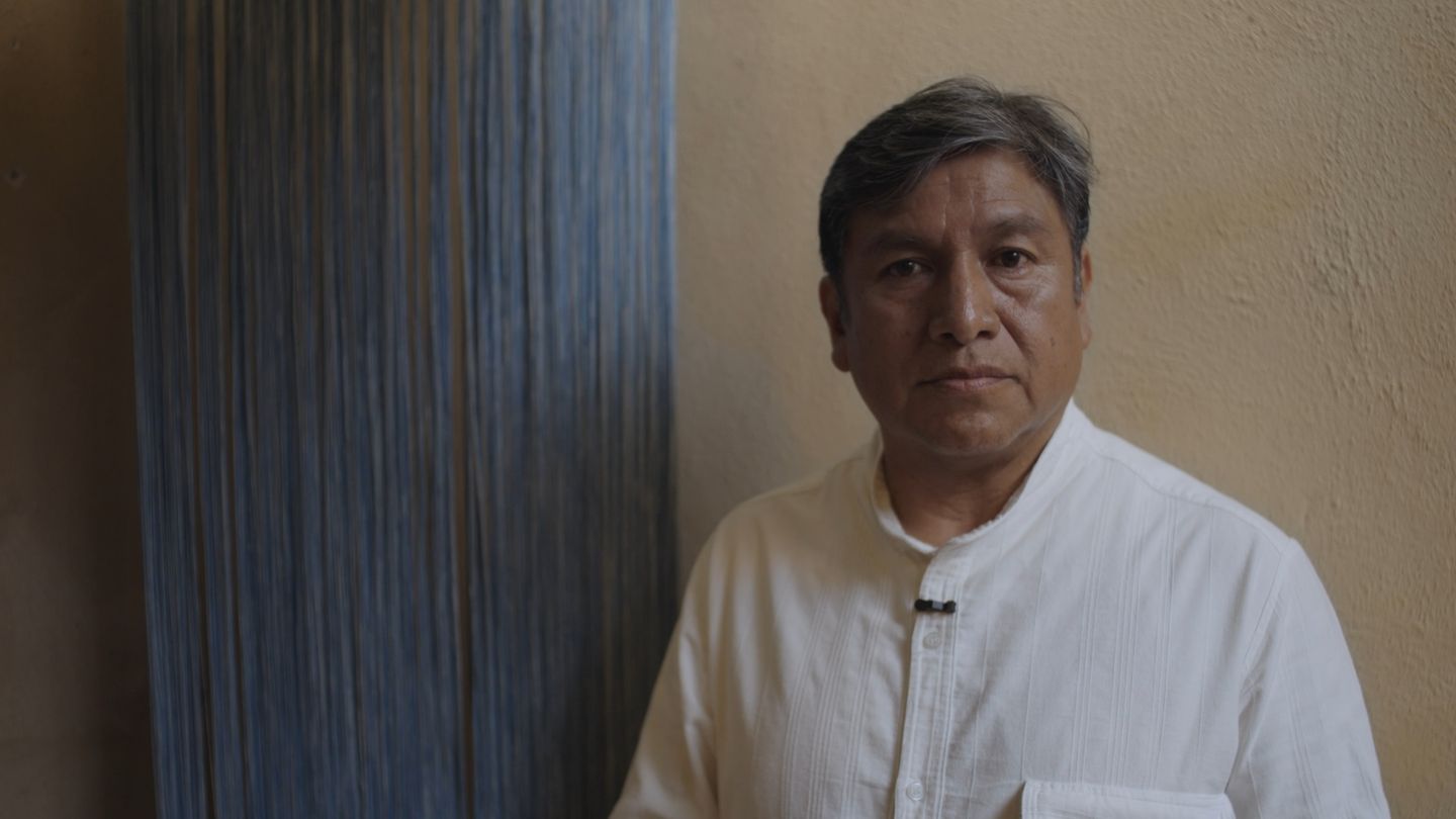 Un hombre de camisa blanca posa junto a una urdimbre tendida.