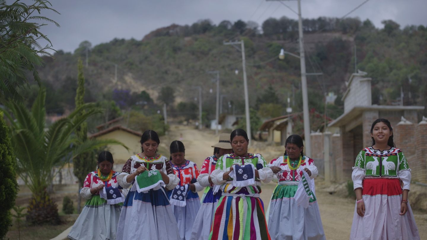 Tres mujeres con trajes tradicionales en el interior de una casa.
