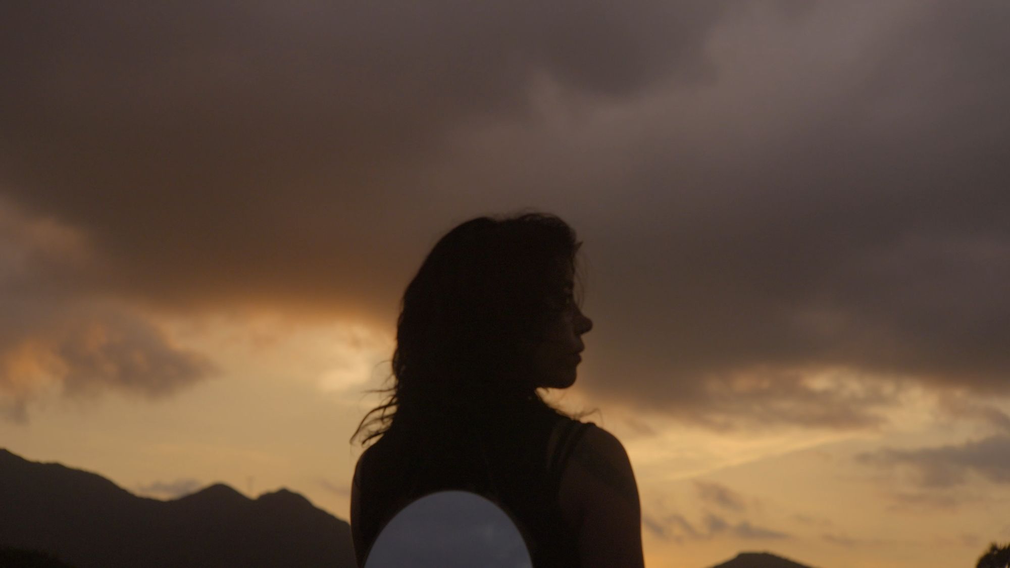 Silueta de una mujer de perfil contra un cielo de nubes al atardecer.