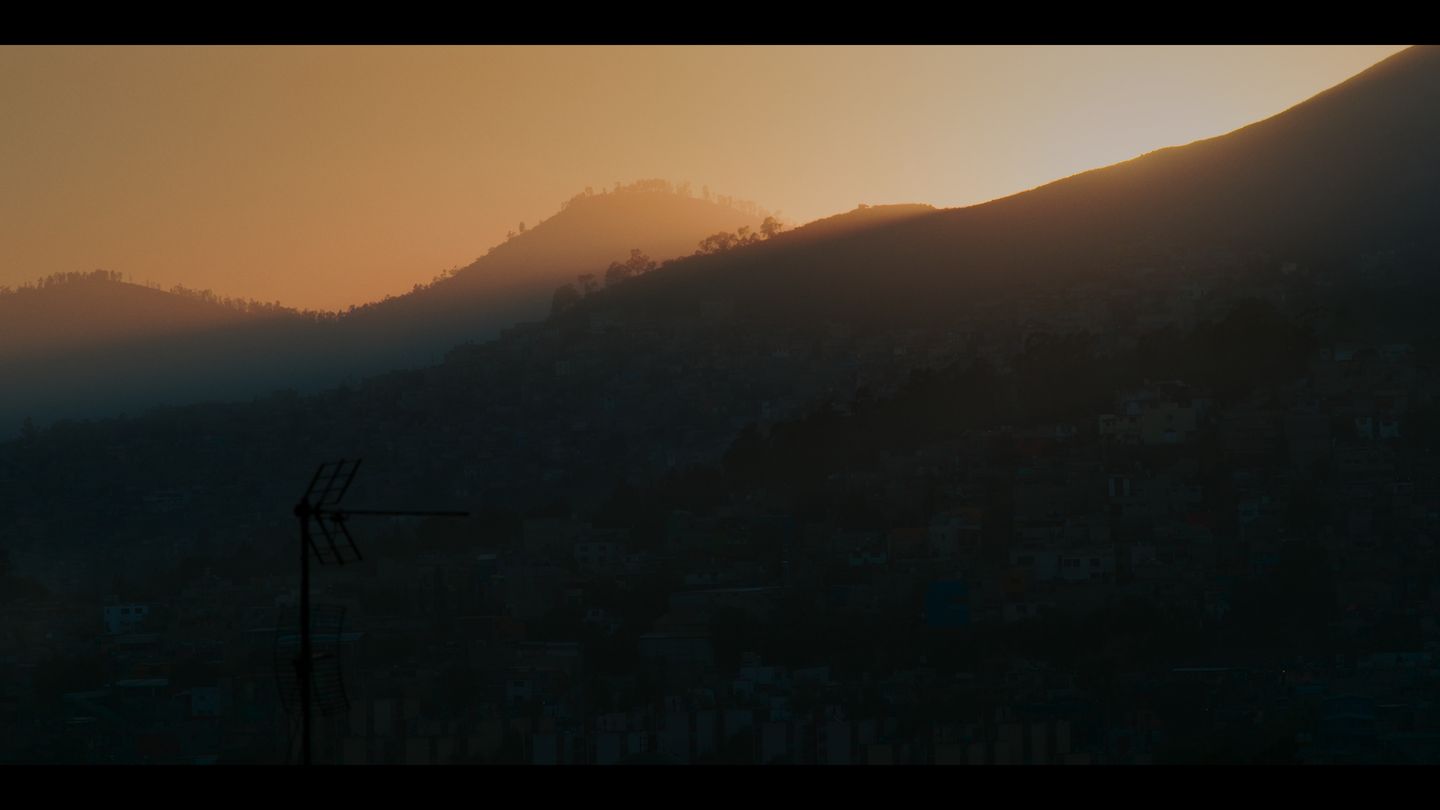 Cordillera al amanecer; el sol asoma tras la silueta de un cerro y el cielo se funde en naranja.