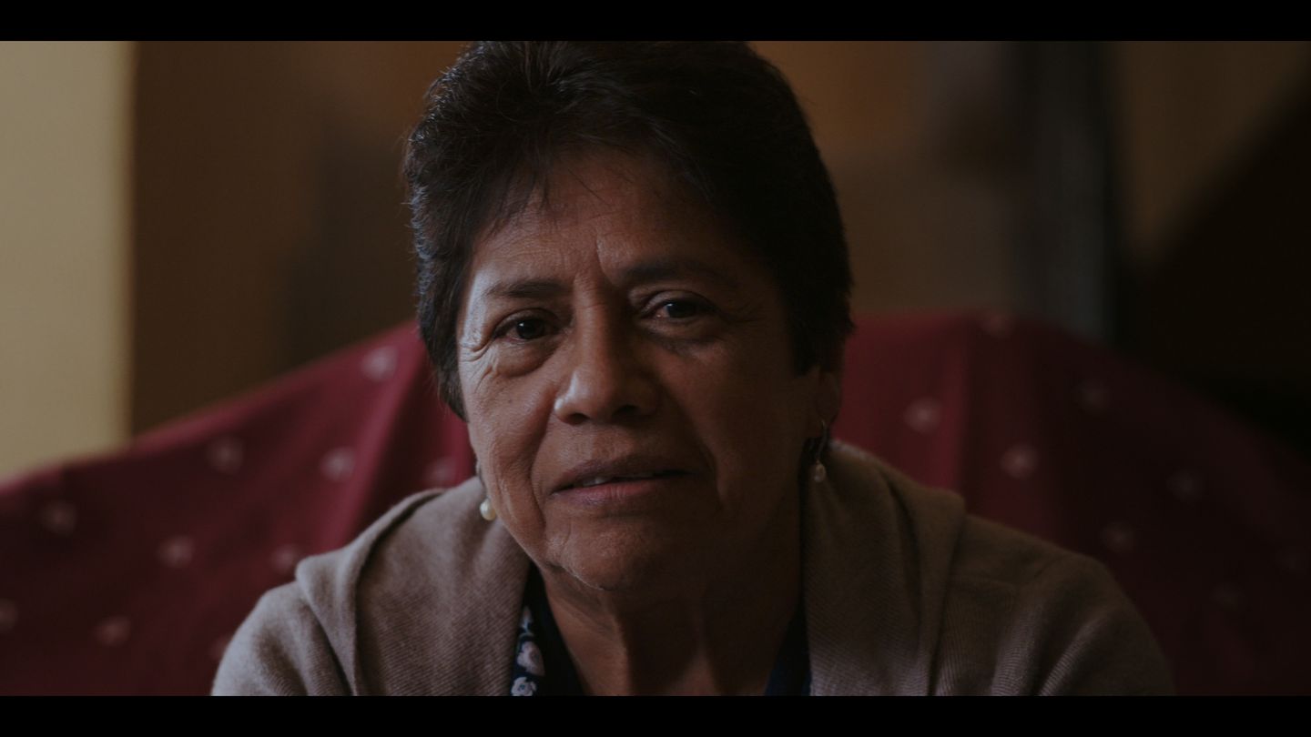Retrato cercano de una mujer mayor en el interior de su casa, luz cálida.