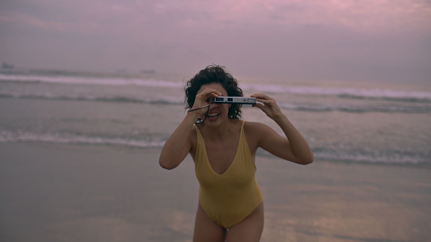 Una niña con traje de baño mira por unos binoculares en una playa al amanecer.