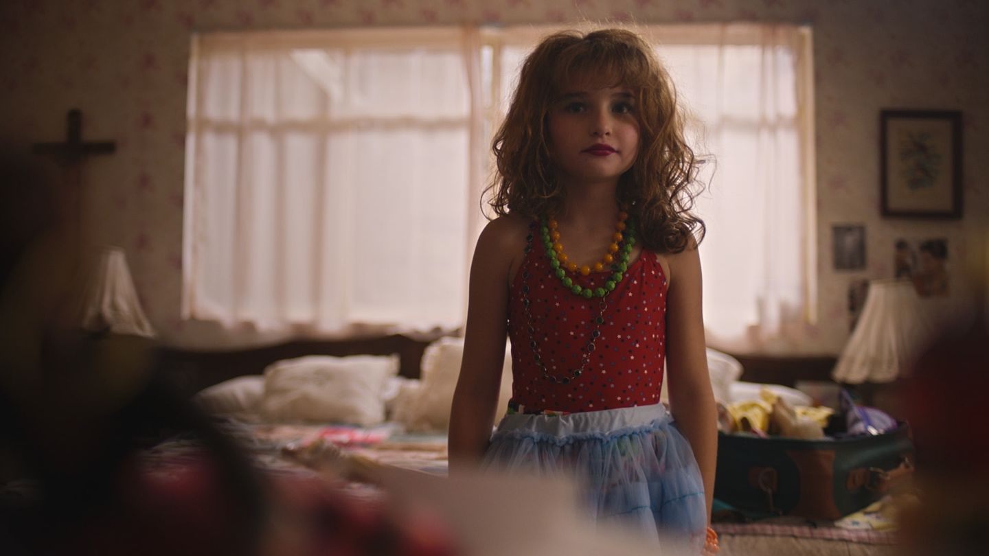 Una niña de pie en una habitación; la luz de la ventana recorta su figura.