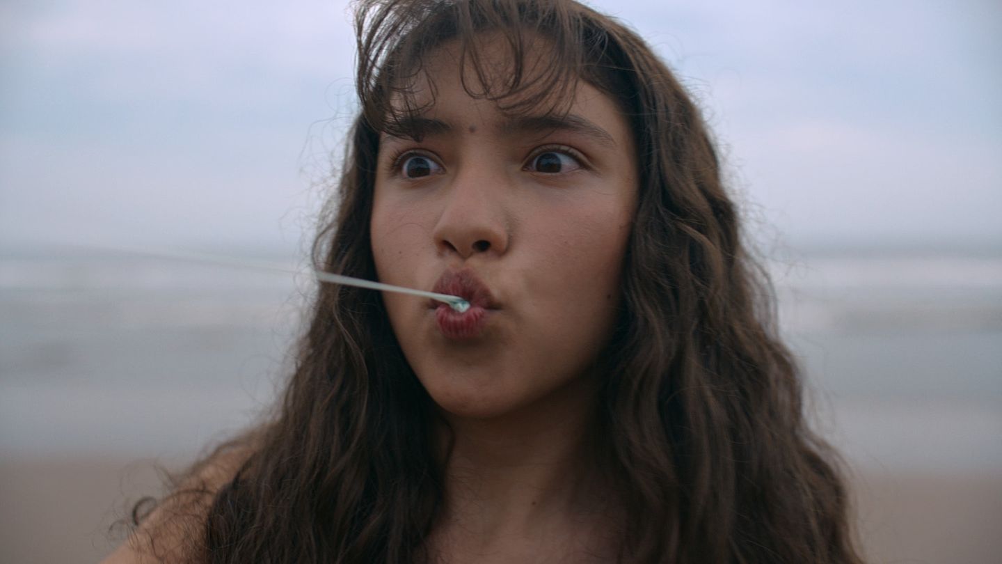 Una niña con un dulce en la boca frente al mar.